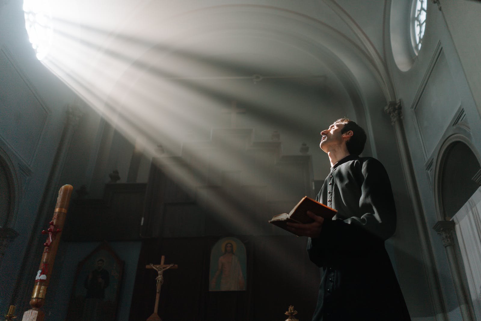 Sunrays Passing Through a Church Window Beside a Priest Holding a Bible