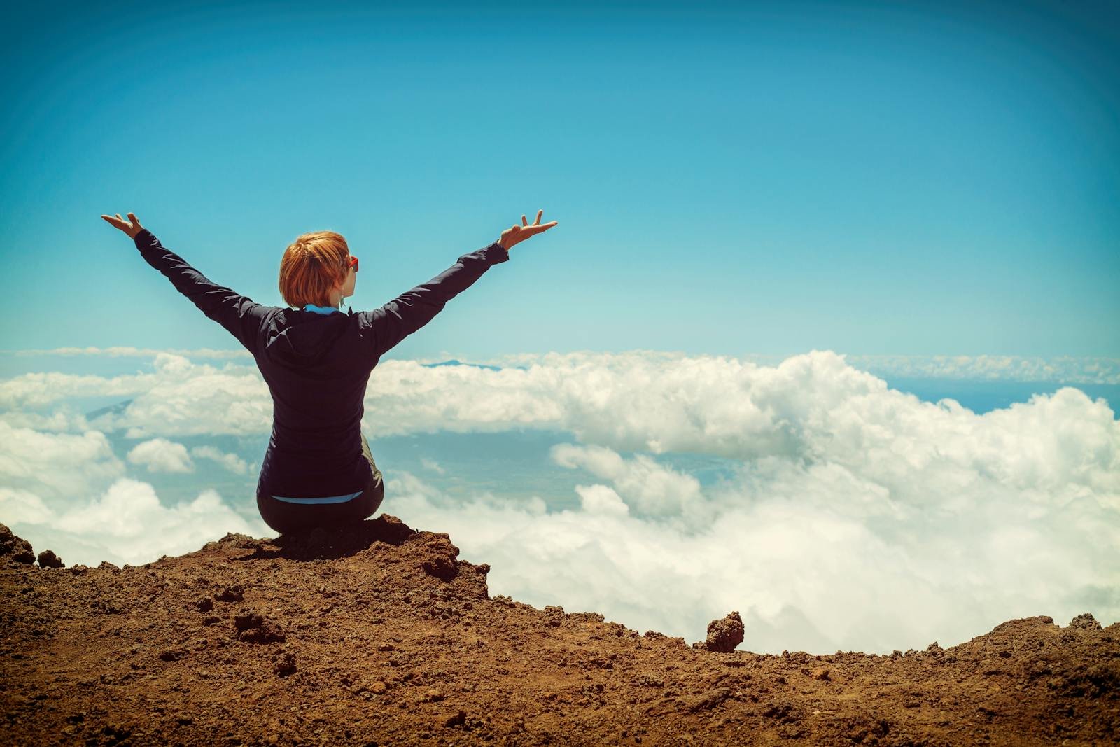 Oración de Acción de Gracias, A woman enjoys a scenic view atop a cliff in Kula, Hawaii, surrounded by clouds and blue sky.