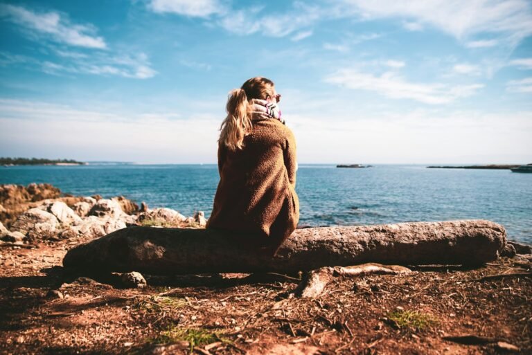 Oración por la Paz Interior, woman in brown sweater sitting on rock near sea during daytime