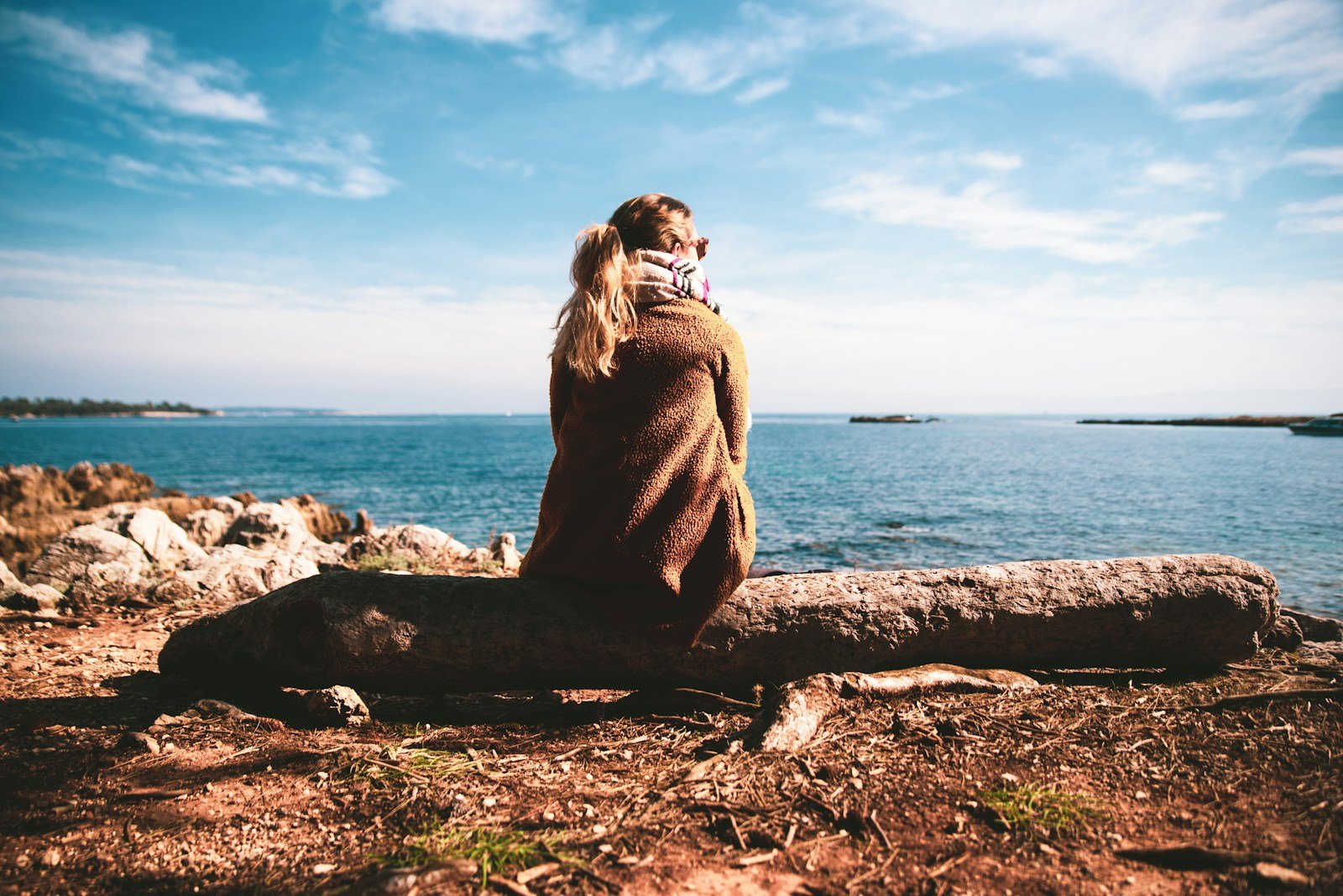 Oración por la Paz Interior, woman in brown sweater sitting on rock near sea during daytime