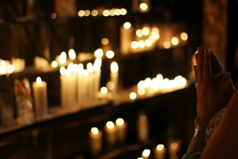 Oración por las Benditas Almas del Purgatorio, Hands clasped in prayer by candlelight in a church in São Paulo, Brazil, evoking a spiritual atmosphere.