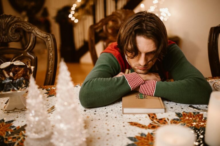 navidad sin quienes amamos, A man in a sweater looks thoughtful and sad at a decorated Christmas table indoors.
